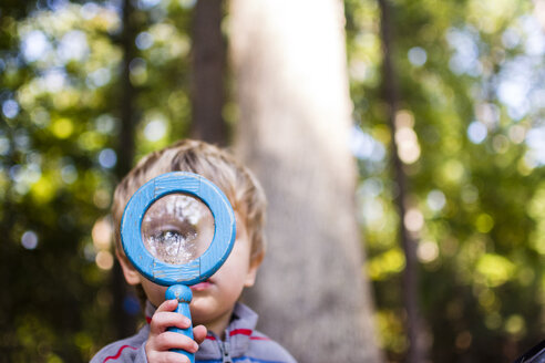 Junge schaut durch ein Vergrößerungsglas, während er im Wald steht - CAVF24772