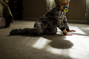 Junge mit Schnuller kniend auf dem Boden zu Hause - CAVF24794