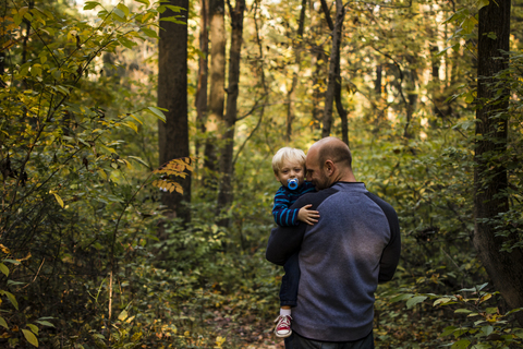 Vater trägt Sohn im Wald stehend, lizenzfreies Stockfoto