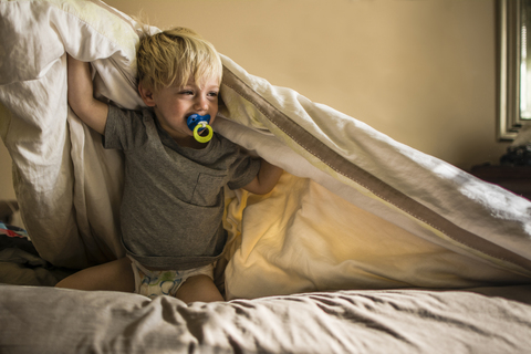 Junge mit Schnuller im Mund, der auf dem Bett kniend weint, lizenzfreies Stockfoto