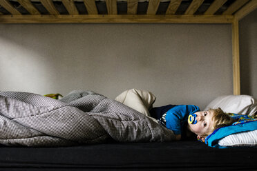 Portrait of boy sucking pacifier while lying on bed - CAVF24811