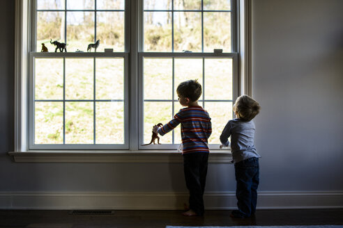 Brüder in voller Länge, die mit Spielzeug spielen, während sie am Fenster stehen - CAVF24812