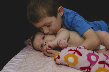 Nahaufnahme eines Jungen, der seine auf dem Bett liegende Schwester küsst, vor schwarzem Hintergrund - CAVF24819