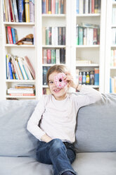 Portrait of laughing little girl with doughnut sitting on couch - LVF06820