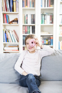 Porträt eines lachenden kleinen Mädchens mit Donut auf der Couch sitzend - LVF06820