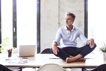 Mature businessman sitting barefoot on desk in office - HAPF02653