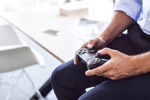Close-up of businessman sitting on desk in office using controller - HAPF02656