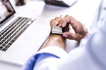 Close-up of businessman at desk with laptop using smartwatch - HAPF02665