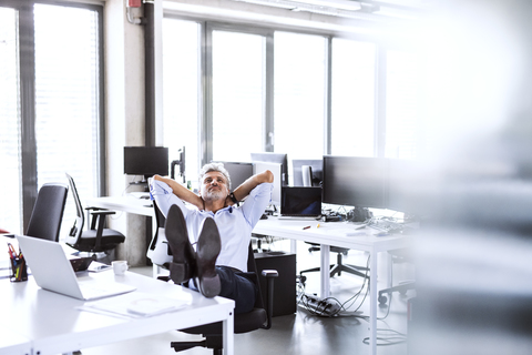 Relaxed mature businessman sitting at desk in office leaning back stock photo