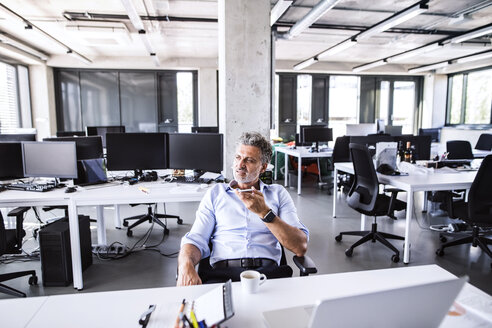 Reifer Geschäftsmann sitzt am Schreibtisch im Büro und benutzt sein Smartphone - HAPF02675