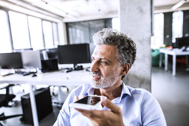 Porträt eines reifen Geschäftsmannes, der im Büro sein Smartphone benutzt - HAPF02676