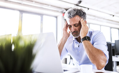 Stressed mature businessman sitting at desk in office with laptop - HAPF02682