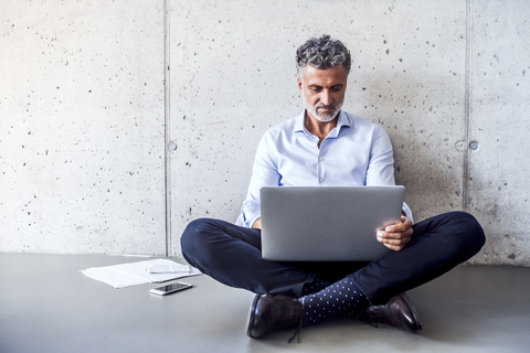 Mature businessman sitting on the floor using laptop stock photo