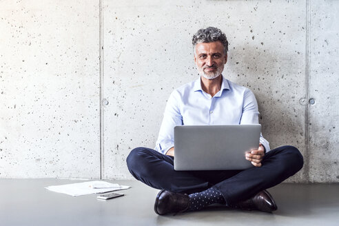 Porträt eines selbstbewussten reifen Geschäftsmannes, der auf dem Boden sitzt und einen Laptop benutzt - HAPF02696