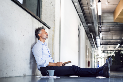 Mature businessman sitting on the floor leaning against the wall stock photo