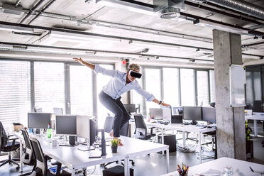 Barfuß reifer Geschäftsmann auf Schreibtisch im Büro mit VR-Brille - HAPF02708
