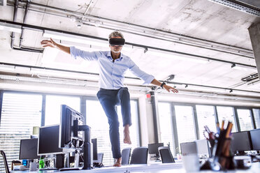 Barfuß reifer Geschäftsmann auf Schreibtisch im Büro mit VR-Brille - HAPF02709