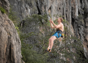 Thailand, Krabi, Lao Liang, barechested climber abseiling from rock wall - ALRF01036