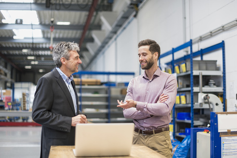 Businessmen using laptop in production hall stock photo