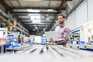 Young businessman using laptop in production hall - DIGF03492