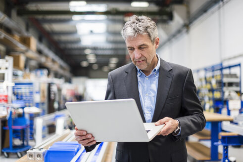 Geschäftsmann mit Laptop in einer Produktionshalle - DIGF03494