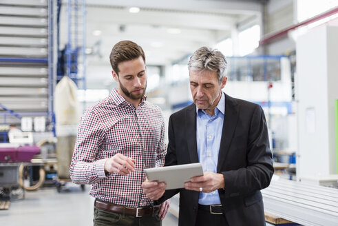 Geschäftsleute benutzen ein Tablet während einer Besprechung in einer Produktionshalle - DIGF03541