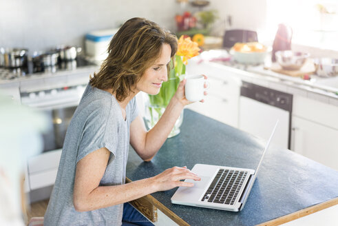 Smiling woman using laptop in kitchen at home - MOEF00930