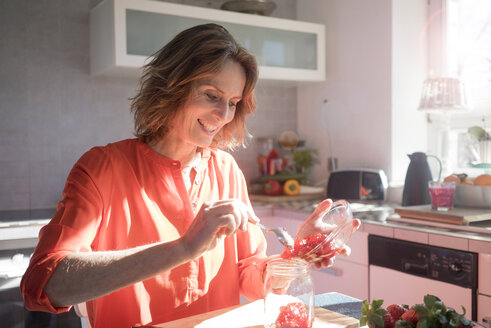 Smiling woman making strawberry jam in kitchen at home - MOEF00934