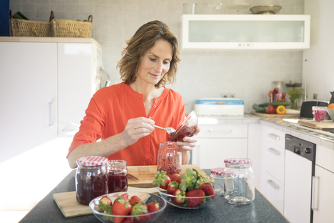 Frau macht Erdbeermarmelade in der Küche zu Hause, lizenzfreies Stockfoto