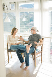 Entspanntes reifes Paar, das sich auf einem Stuhl zu Hause unterhält - MOEF00942