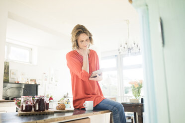 Frau mit Tablet und selbstgemachter Erdbeermarmelade zu Hause - MOEF00943