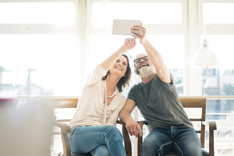 Happy mature couple sitting on chairs at home using tablet stock photo