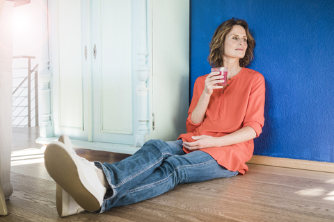 Entspannte Frau, die zu Hause mit einem gesunden Getränk auf dem Boden sitzt, lizenzfreies Stockfoto