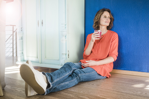 Relaxed woman sitting on the floor at home with healthy drink stock photo