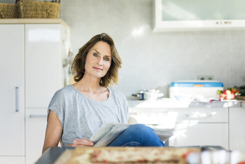 Portrait of woman with newspaper in kitchen at home - MOEF00950