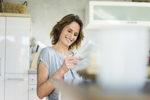 Lächelnde Frau liest Zeitung in der Küche zu Hause, lizenzfreies Stockfoto