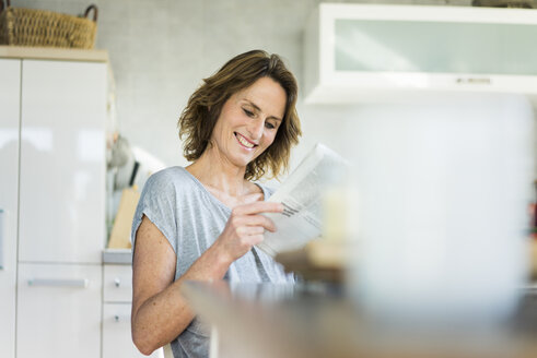 Lächelnde Frau liest Zeitung in der Küche zu Hause - MOEF00951