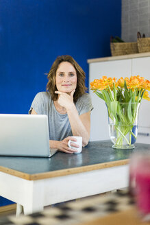 Portrait of smiling woman with laptop in kitchen at home - MOEF00957