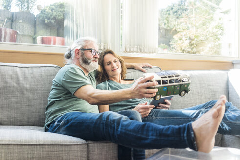 Mature couple on couch at home holding minibus model - MOEF00958