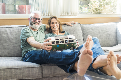 Glückliches reifes Paar auf der Couch zu Hause mit einem Kleinbusmodell, lizenzfreies Stockfoto