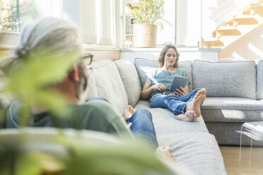 Mature couple relaxing on couch at home with woman holding tablet - MOEF00966