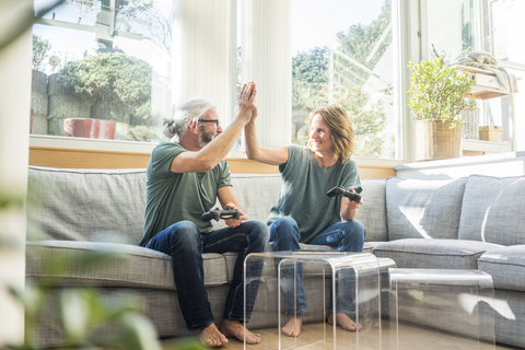 Happy mature couple sitting on couch at home playing video game stock photo