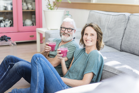 Happy mature couple with healthy drinks in living room at home stock photo