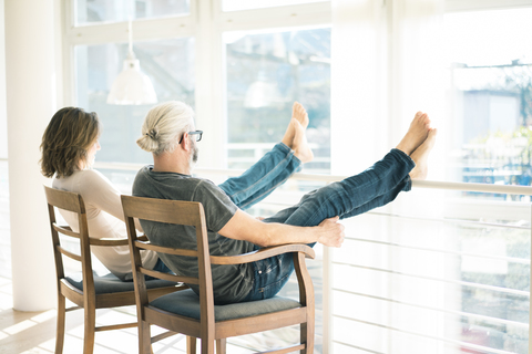 Entspanntes reifes Paar sitzt auf Stühlen zu Hause und legt die Füße hoch, lizenzfreies Stockfoto