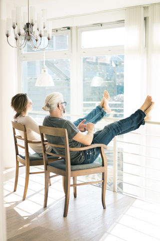 Relaxed mature couple sitting on chairs at home with feet up stock photo