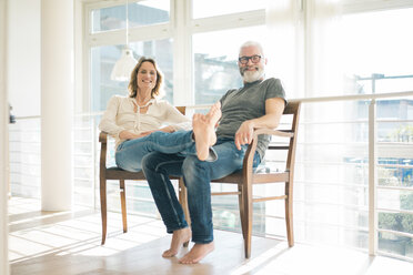 Porträt eines entspannten reifen Paares, das zu Hause auf einem Stuhl sitzt - MOEF00990