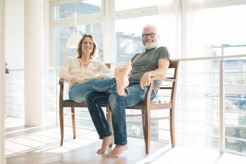 Portrait of relaxed mature couple sitting on chairs at home - MOEF00990