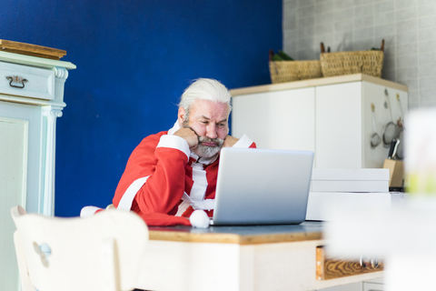 Frustrierter Weihnachtsmann benutzt Laptop zu Hause, lizenzfreies Stockfoto