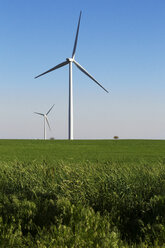 Windmühlen auf einem grasbewachsenen Feld vor blauem Himmel - CAVF24935