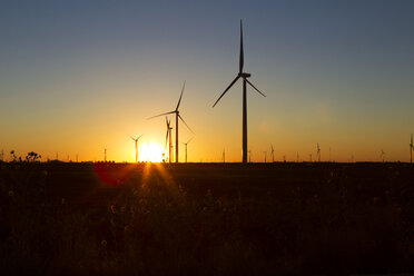 Silhouette windmills on field against orange sky during sunset - CAVF24937